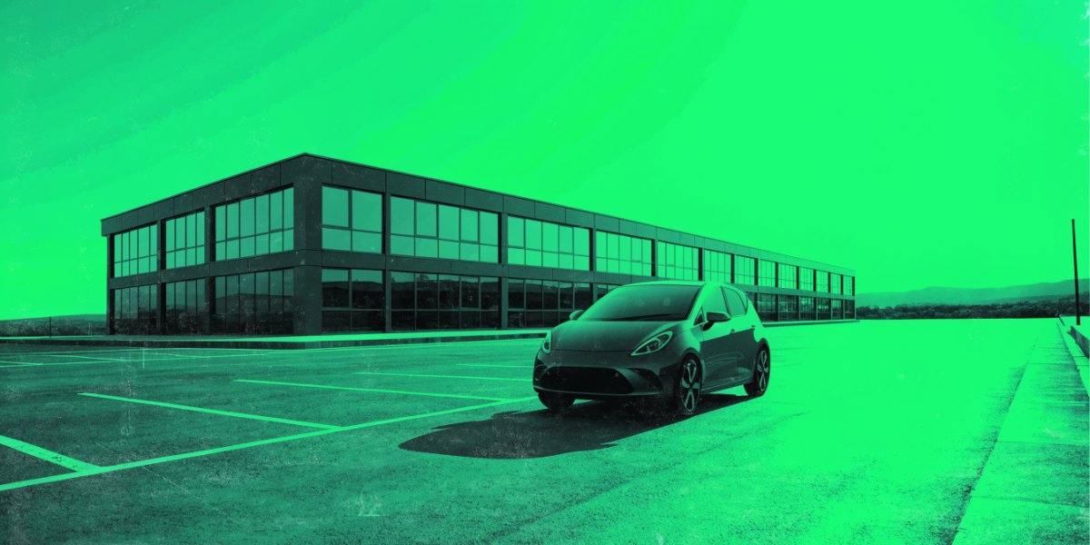 A small modern electric city hatchback in an open-air car park beside a low contemporary office building in soft morning light