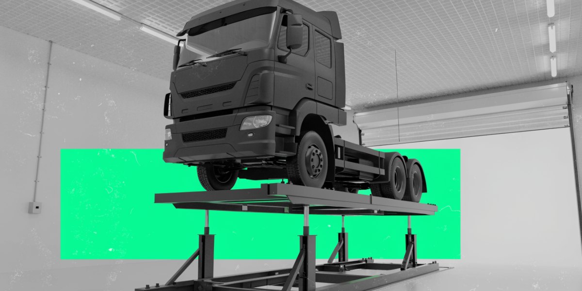 A heavy truck raised on a workshop inspection lift in a clean, well-lit commercial vehicle inspection bay